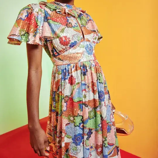 Model posed in glittery, floral Celeste Dress from Celia B. Print is primarily orange, green, red, and blue.