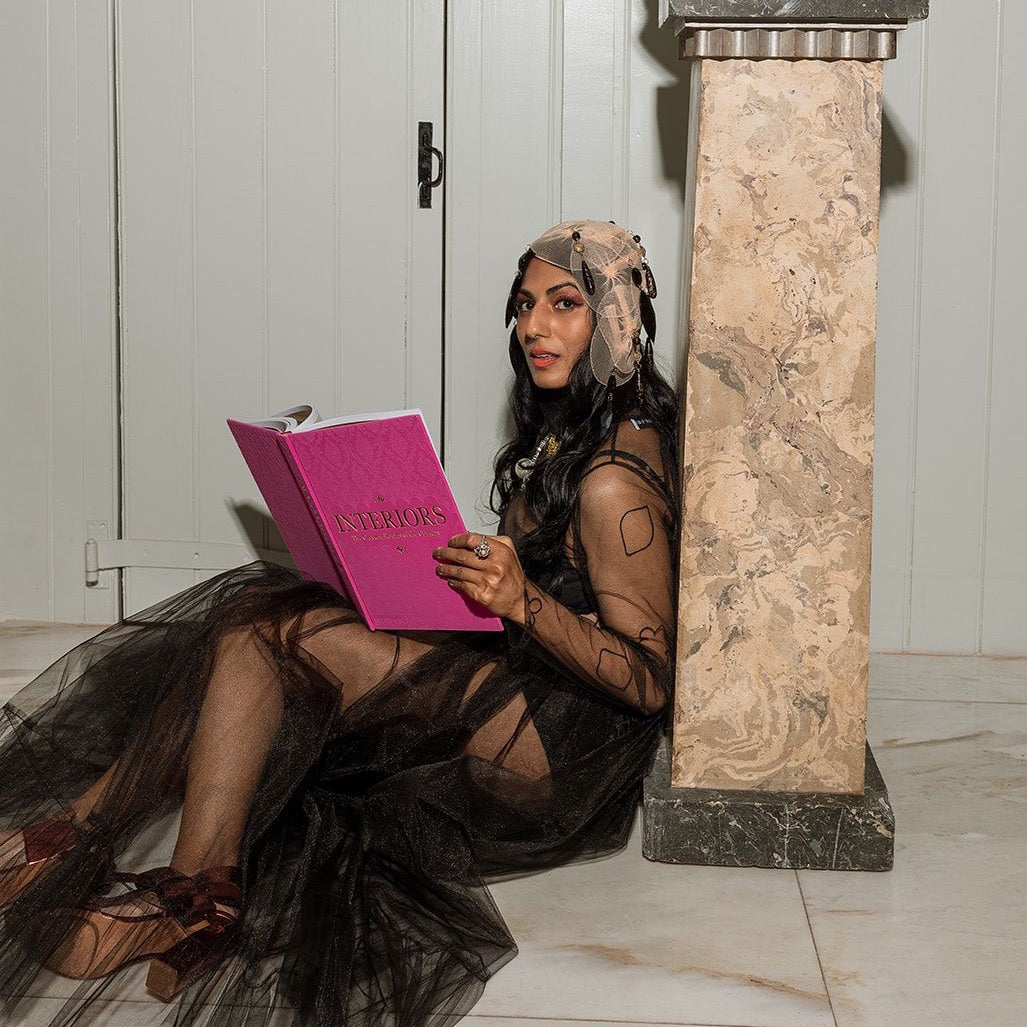 Saint Claude Social Club Muse reading Interiors: The Greatest Rooms of the Century (Pink Edition) wearing black embroidered tulle blouse and black tulle skirt from Mehtap Elaidi.