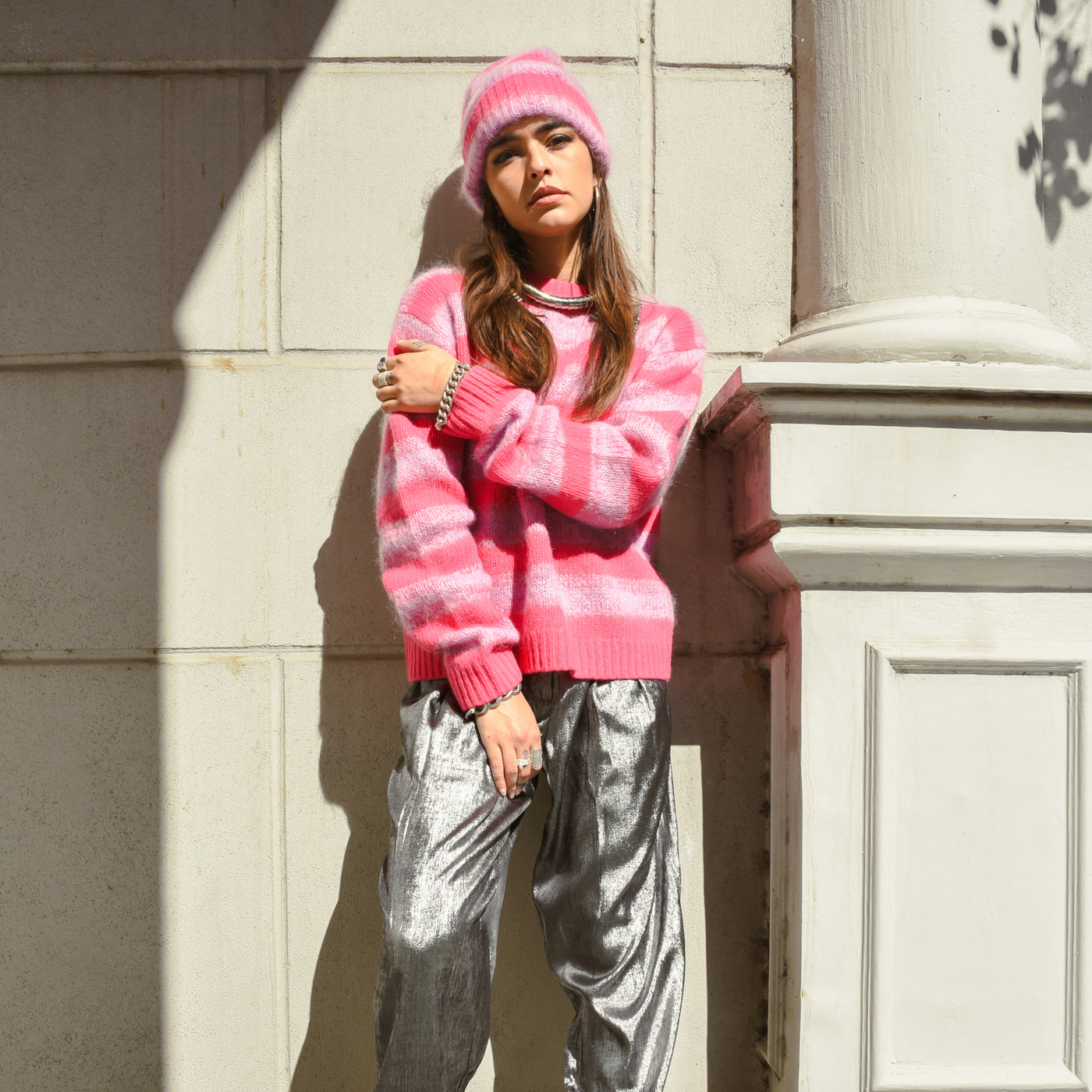 Model is posed in the pink Wool Mix Sweater, Wool Mix Hat, and Silver Shiny Pants all from Stella Nova. Model wears jewelry from Saint Claude.