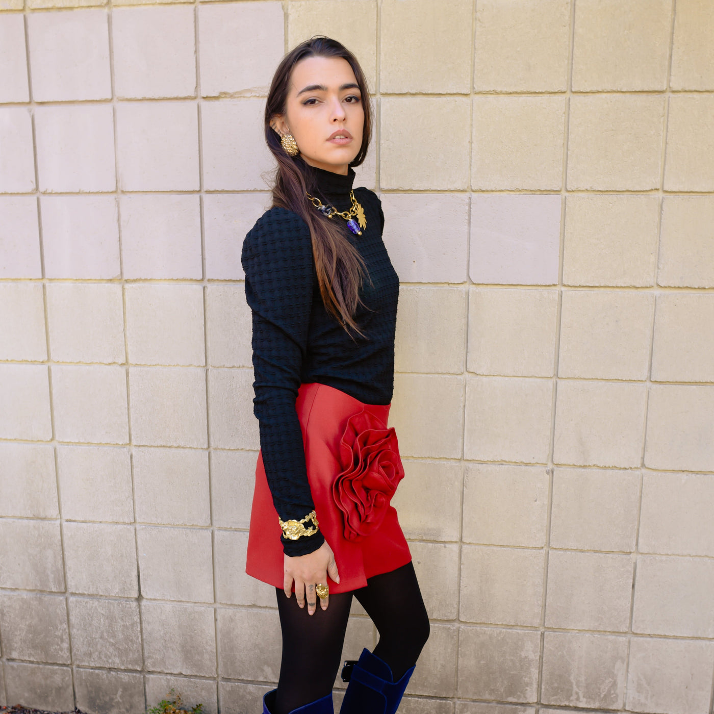Model posed in the black Turtleneck Blouse and Fabrizia Wool Blend Mini Skirt. Model wears jewelry from Saint Claude.